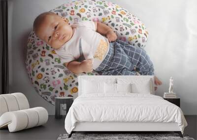 Portrait of a two month old boy looking at camera cutely and smiling as he sleeps in brown clothes in newborn baby photo shoot
 Wall mural