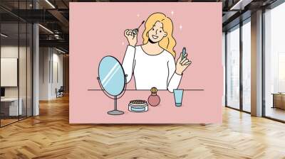 Smiling girl sit at table doing makeup put mascara. Happy young woman look in mirror apply beauty cosmetics products. Daily routine and preparation. Cosmetology. Vector illustration.  Wall mural