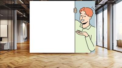 Smiling young man look behind mockup white poster show good deal or offer. Happy male recommend promotion on empty placard. Copy space. Vector illustration.  Wall mural