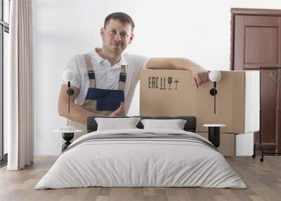 Relocation service man holds thumb up. Mover with cardboard boxes Wall mural