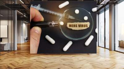 A man looks through a magnifying glass at pills, a syringe and a piece of paper with the inscription - MERS virus Wall mural