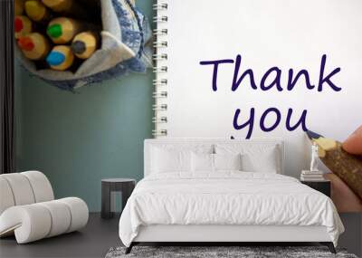 Hand writing 'thank you', isolated on blue background. Bag with pencils. Wall mural