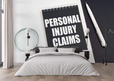 On a black and white surface lies a magnifying glass, a pen and a notepad with the inscription - Personal Injury Claims Wall mural