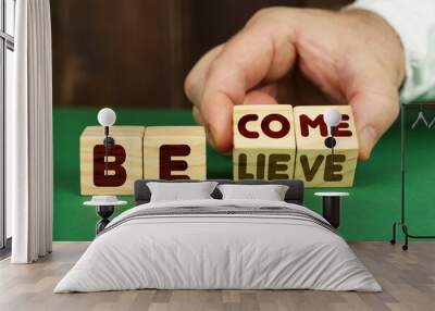 On a green surface, a man puts cubes with the inscription - BECOME, BELIEVE Wall mural