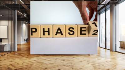 Time for Phase 2. Hand is turning a cube and changes the word 'Phase 1' to 'Phase 2'. Beautiful white background. Business concept. Copy space. Wall mural