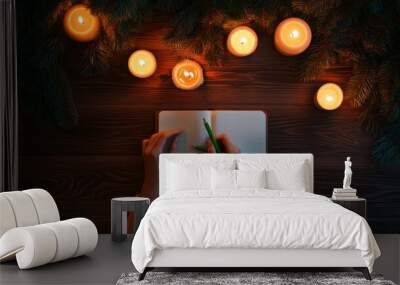 Winter scene, person writing in notebook surrounded by pine branches and candles. Wall mural