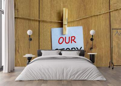 Wooden clothespin with white sheet of paper. Text 'our story'. Beautiful wooden background. Business concept, copy space. Wall mural