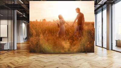 The couple go on a field at sunset holding hands Wall mural