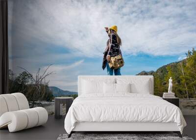 woman in blue jeans and Hiking bag stands on the shore of a mountain lake and looking into the distance Wall mural