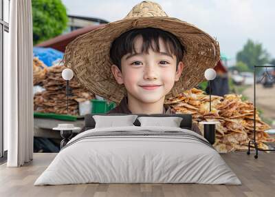 A young boy wearing a straw hat is smiling at the camera. He is standing in front of a pile of food, which suggests that he might be selling or preparing food. The scene has a casual Wall mural