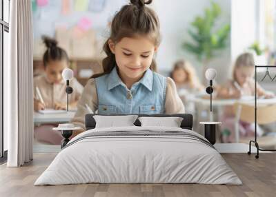 A young school girl smiles as she writes in her notebook during class.  The other students are blurred in the background. Wall mural