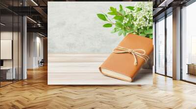 Explore the serene beauty of a brown leather notebook paired with a vibrant bouquet of greenery creating a perfect aesthetic for relaxation and creativity Wall mural