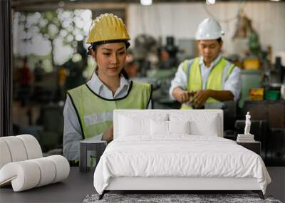 Asian woman engineer industry heavy worker wearing hardhat and holding tablet looking camera standing at machine area in factory, factory industrial concept. Wall mural