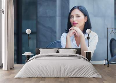 Beautiful businesswoman sitting at cafe, looking at camera. Wall mural