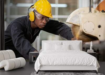 Black male african american workers wear sound proof headphones and yellow helmet working an iron cutting machine in factory Industrial. Wall mural