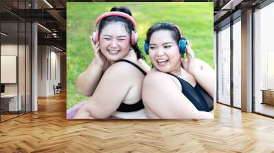 Cheerful laugh smiling friends young asian woman happy wear headphone listen to music in sportswear walking after exercise. Two sporty women body curvy positive having fun workout in garden. Wall mural