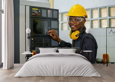 Engineering male african american workers wear soundproof headphones and yellow helmet working at operating CNC machine. work factory industrial concept. Wall mural