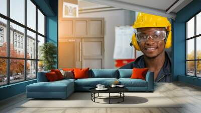 Engineering male african american workers wear soundproof headphones and yellow helmet working at operating CNC machine. work factory industrial concept. Wall mural