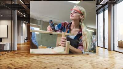 Female carpenter wear goggles using woodworking drill to make furniture. carpenter woman using electric drill machine at workplace. Wall mural