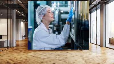 Female worker using laptop checking quality drinking water management system before process of filling water into bottles to bring out to consumers. Water production line of factory. Wall mural