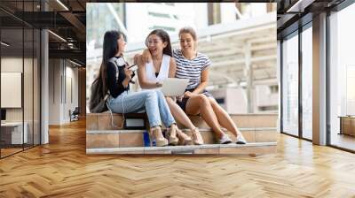 group of beautiful women having fun and using laptop sitting at city. Wall mural