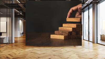 Close-up hand is placing wood block tower stacked in stair step with caution to prevent collapse or crash concepts of financial risk management and strategic planning. Wall mural