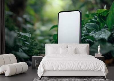 A blank smartphone stands among lush green foliage, ideal for showcasing app designs or nature-themed projects. Wall mural