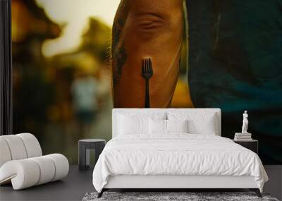 A close-up of a man's arm with a tattoo of a fork, symbolizing culinary passion and personal expression. Wall mural