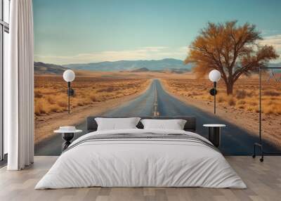 A tranquil desert road stretches into the horizon beneath a clear blue sky, flanked by dry landscapes and a solitary tree. Wall mural