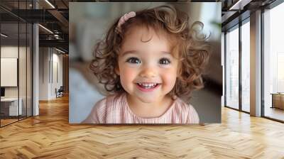 Cheerful little girl with curly hair and a bright smile, exuding joy in a warm, cozy environment. Wall mural