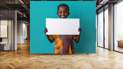 A young boy is holding a blank white sign. The boy is smiling and he is happy. The sign is white and has no writing on it. Concept of innocence and joy Wall mural