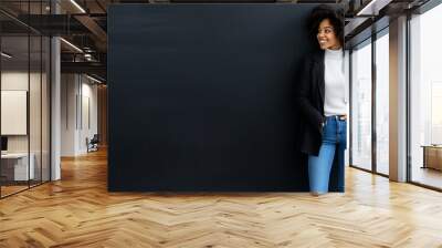  Young, laidback, and stylish black female entrepreneur in jeans and blazer smiling on isolated dark background with copy space. Wall mural