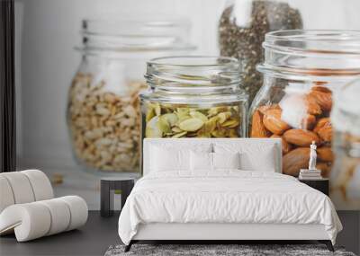 Various nuts and seeds in glass jars over white wooden table against white background. The concept of vegetarian and organic food. Set of photos. Wall mural