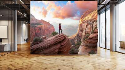 Adventurous Woman at the edge of a cliff is looking at a beautiful landscape view in the Canyon during a vibrant sunset. Taken in Zion National Park, Utah, United States. Sky Composite. Wall mural