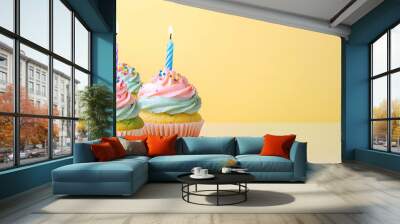 Close-up shot of two cupcakes with pink and green frosting and lit candles on a yellow background. Wall mural