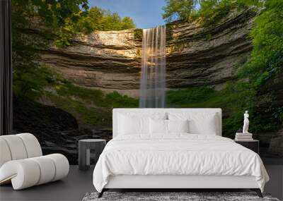 Majestic waterfall cascading down a cliff face in a lush forest setting. Wall mural