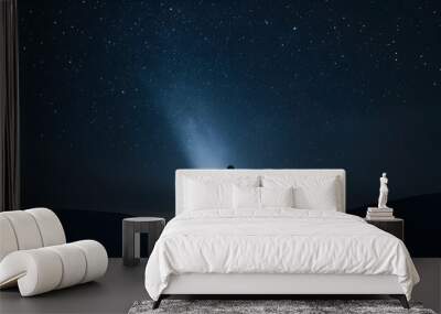 Silhouette of a person standing in a starry night with a beam of light shining up. Wall mural