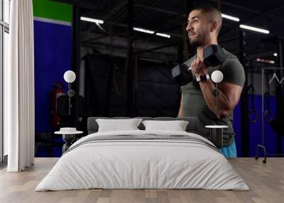 latino man with sportswear doing biceps exercises with two dumbbells in a gym Wall mural