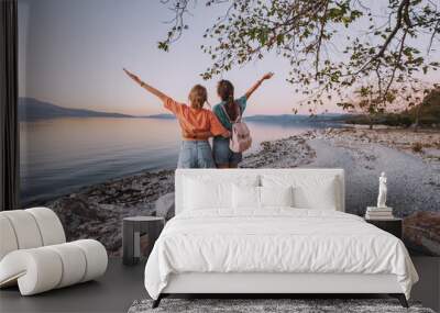 A couple of friends girls are traveling and enjoying the view of the lake or sea coast. Wall mural