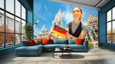 A happy girl with a German flag poses against the background of the city hall in Munich. Travel and immigration to Germany Wall mural