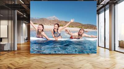 A multinational group of three friends of students laugh and swim in the sea with a board near the beach. Concept of travel and friendship Wall mural