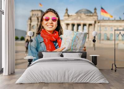 Beautiful young woman looking at map guide while standing in front of Bundestag building at sunset in Berlin. Travel in Germany concept Wall mural