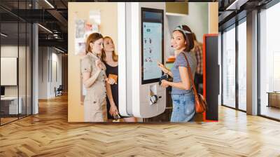 Group of people, friends ordering food at the touch screen self service terminal by the electronic menu in the fastfood restaurant Wall mural