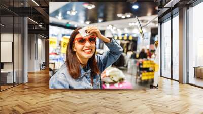 Happy eastern woman buying and choosing stylish sunglasses in shop in the Mall Wall mural