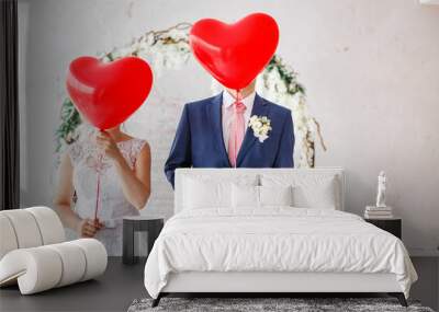 Happy groom and bride covered their faces with red balloons at wedding party indoors Wall mural