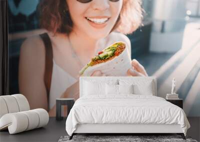 Happy woman eats a fast food flatbread with filling sitting on the street and resting after a working day. Concept of healthy food and extra calories Wall mural