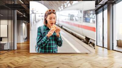 Healthy young woman biting her hamburger at railway station near fast train Wall mural