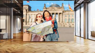 Multiracial group of friends visiting the city of Berlin. Two women reading map with Reichstag building on the background. Friendship and travel concept with real candid emotions Wall mural