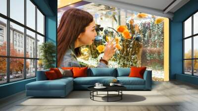 Smiling young brunette woman looking at fish in aquarium Wall mural