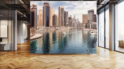 The boat sails along the canal in the Dubai Marina area against the backdrop of numerous residential skyscrapers and hotels Wall mural